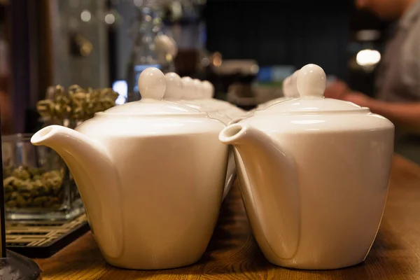 Many white ceramic teapots with round lids stand on the wooden bar counter in the restaurant. Concept dishes in cafe, tea, breakfast