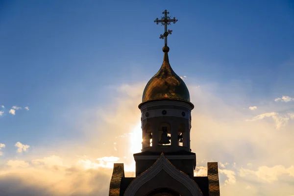 Old Christian chapel in Kemerovo with golden and gilded domes, brown granite walls against a sky and sunset. Concept of faith in god, orthodoxy, prayer