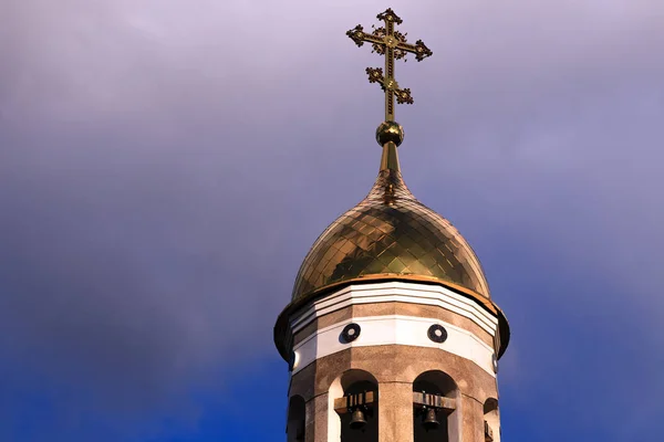 Old Christian chapel in Kemerovo with golden and gilded domes, brown granite walls against a sky and sunset. Concept of faith in god, orthodoxy, prayer