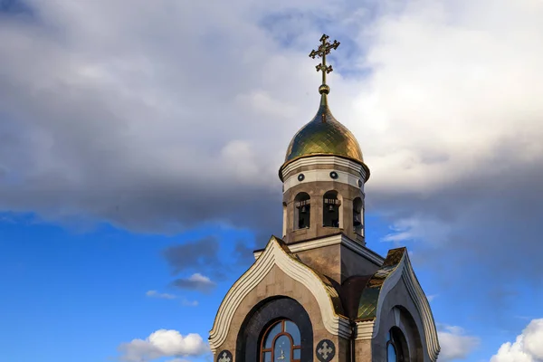 Old Christian chapel in Kemerovo with golden and gilded domes, brown granite walls against a sky and sunset. Concept of faith in god, orthodoxy, prayer