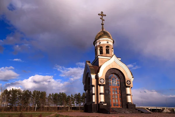 Old Christian chapel in Kemerovo with golden and gilded domes, brown granite walls and glass doors against a blue sky, beautiful autumn landscape. Concept of faith in god, orthodoxy, prayer
