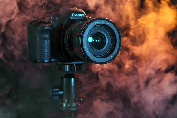 Russia, Novosibirsk, 29 October 2018. Close-up of a professional camera on a tripod in the studio on a black background and white and colorful smoke. Concept photo shoot video recording