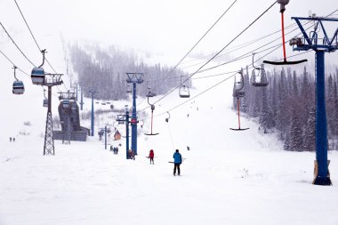 Ski lift kayakçılar, snowboard, karla kaplı dağlar, kar fırtınaları, yaprak dökmeyen ağaçlar arka plan üzerine açık kabin ile teleferik füniküler üzerinde. Alpler resort, Georgia, Sochi kavramı