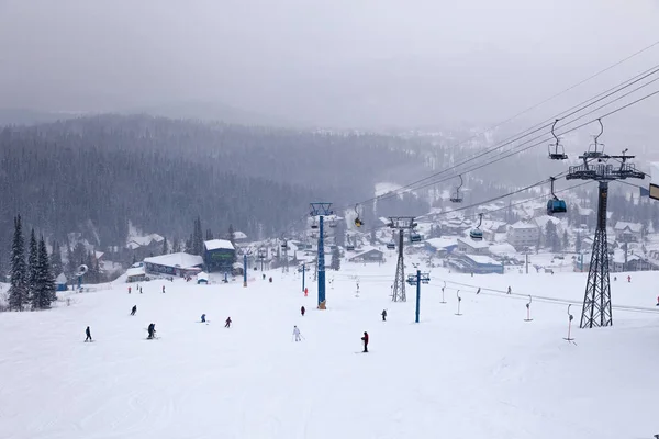 Ski lift on the cable car funicular with open cabin on the background of skiers, snowboarders, snow-capped mountains, blizzards, evergreen trees. Concept of Alps resort, Georgia, Sochi