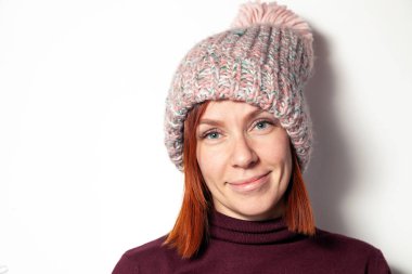 Güzel genç Kızıl saçlı kız mor kazak ve pembe örme şapka giymiş ponpon Studio beyaz arka plan üzerinde yana doğru gülümseyen izole portresi. Kapaklar örgü konsept mağaza