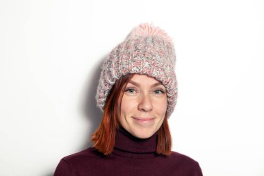 Mor kazaklı yeşil gözlü güzel genç Kızıl saçlı kız ve pembe örme şapka giymiş ponpon Studio beyaz arka plan üzerinde yana doğru gülümseyen izole portresi. Kavram örgü Dergisi