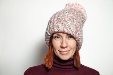 Mor kazaklı yeşil gözlü güzel genç Kızıl saçlı kız ve pembe örme şapka giymiş ponpon Studio beyaz arka plan üzerinde yana doğru gülümseyen izole portresi