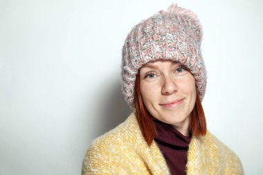 Güzel genç Kızıl saçlı kız yeşil gözleri mor sarı kazaklı ve pembe örme şapka giymiş ponpon beyaz arka plan studio yana doğru gülümseyen izole portresi. Kavram örgü Dergisi