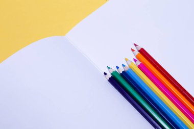 Seamless colored rainbow pencils on sheets of white paper school drawing album on yellow  background isolated.   Concept of free space, copyspace, cover of notebook use for professional drawin