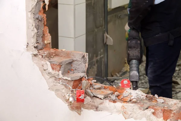 Man professional worker in dusty uniform breaks brick, concrete walls and tile with perforator. Concept overhaul, renovation, redevelopment of the walls of the office, kitchen in restaurant