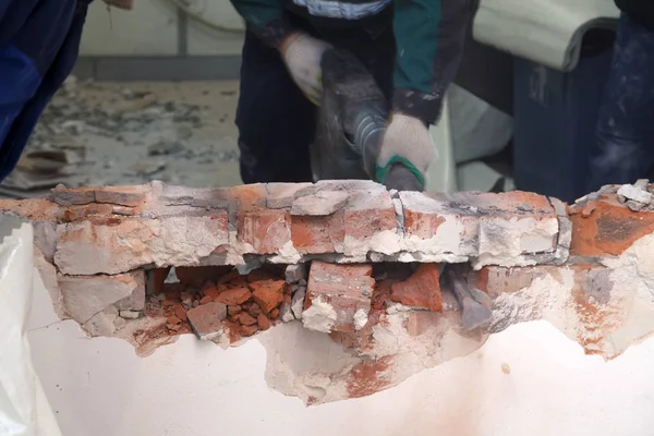 Man professional worker in dusty uniform breaks brick, concrete walls and tile with perforator. Concept overhaul, renovation, redevelopment of the walls of the office, kitchen in restaurant