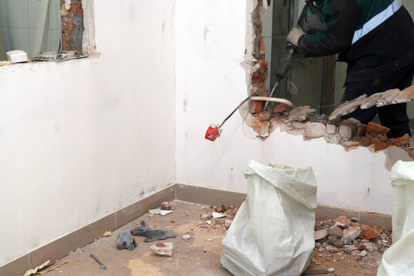 Man professional worker in dusty uniform breaks brick, concrete walls and tile with perforator. Concept overhaul, renovation, redevelopment of the walls of the office, kitchen in restaurant