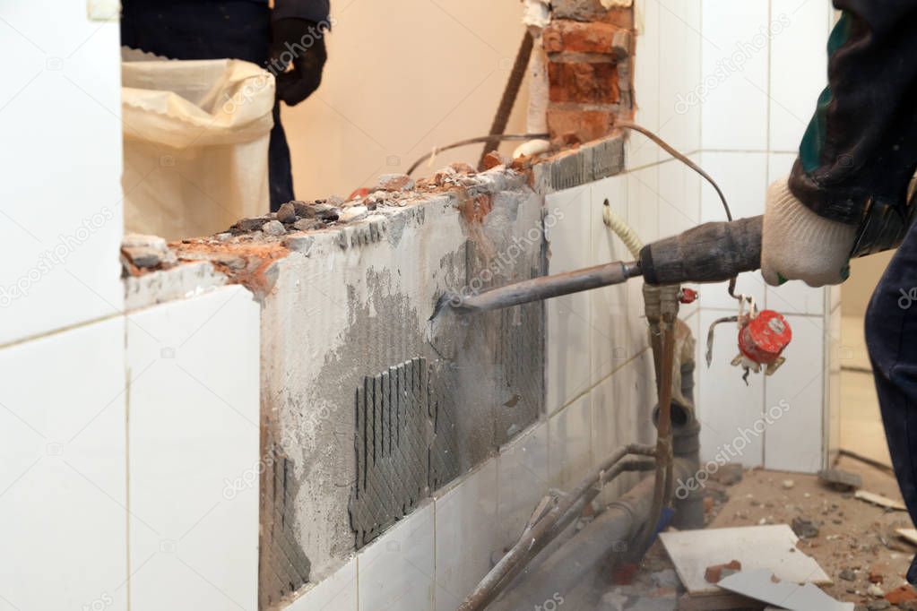 Man professional worker in dusty uniform breaks brick, concrete walls and tile with perforator. Concept overhaul, renovation, redevelopment of the walls of the office, kitchen in restaurant