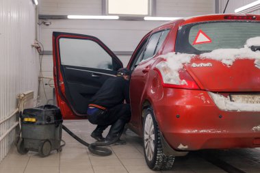 Rusya Kemerovo 2019-01-05 Autowasherman temiz Suzuki Swift parlak kırmızı küçük araba ile elektrikli süpürge, profesyonel kimyasal deterjan kir karda. Dış, iç için kapsamlı bakım kavramı
