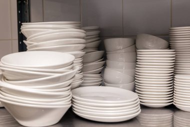 Restoranın arkasındaki metal bir rafta beyaz, seramik porselen tabaklar yığını. Ziyafet, yemek ve açık büfe hazırlığı kavramı