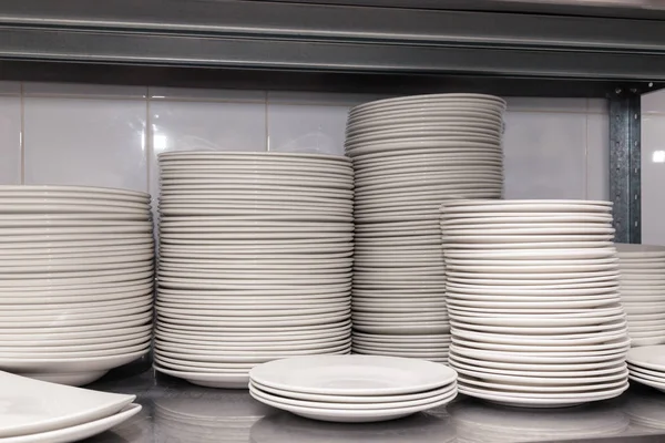 Restoranın arkasındaki metal bir rafta beyaz, seramik porselen tabaklar yığını. Ziyafet, yemek ve açık büfe hazırlığı kavramı