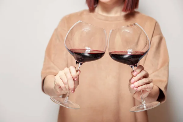 Redhaired girl sommelier on white background and hold with two glasses of red wine. Concept alcoholism, alcohol addiction, bad habit, collection rare wines, blind degustation