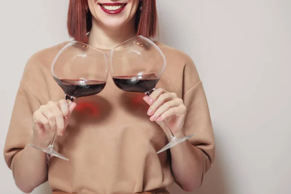 Redhaired girl sommelier on white background and hold with two glasses of red wine. Concept alcoholism, alcohol addiction, bad habit, collection rare wines, blind degustation