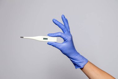 Kapalı el lastik lateks tıp eldiveninde beyaz bir elektronik termometre tutuyor. Beyaz arka planda izole edilmiş. Kavrama sıcaklığı, ateşi, acıyı, rahatsızlığı