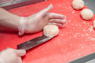 Şef eldiven giymiş, bıçakla tavuk pirzolası yapıyor.