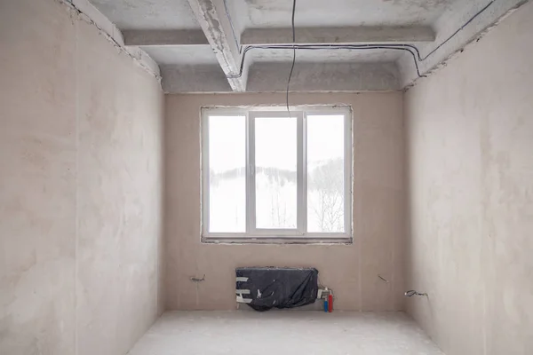 Empty room with a window and a battery in a house under construc
