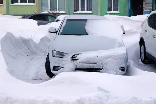 Автомобиль, покрытый снегом, стоит на стоянке жилого дома зимой. Из-за непогоды, снегопада, сложных погодных условий, морозов, метели, не запустился двигатель автомобиля — стоковое фото
