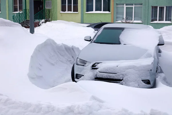 Автомобиль, покрытый снегом, стоит на стоянке жилого дома зимой. Из-за непогоды, снегопада, сложных погодных условий, морозов, метели, не запустился двигатель автомобиля — стоковое фото