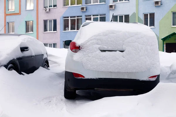 Car covered with snow stands in parking lot of residential building in winter. oncept of bad weather, snowfall, harsh weather conditions, frost, blizzard, car engine did not start