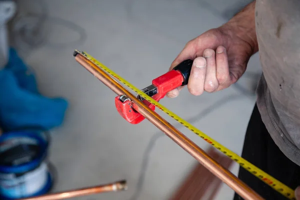 Tukang ledeng pekerja tertutup mengukur pipa tembaga dengan pita roulette, pemotong pipa. Pemasangan konsep, penggantian jalur pipa, perbaikan profesional, kebocoran, pelepasan limbah — Stok Foto