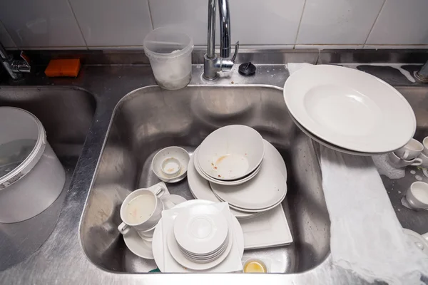 Closeup stack of dirty dishes at bottom of metal square sink