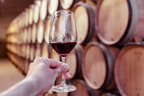 Closeup hand with glass of red wine on background wooden oak bar