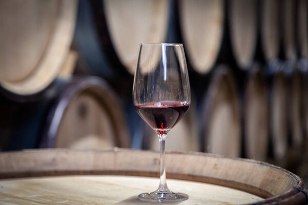 Closeup glass with red wine on background wooden wine oak barrel