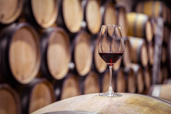 Closeup glass with red wine on background wooden wine oak barrel