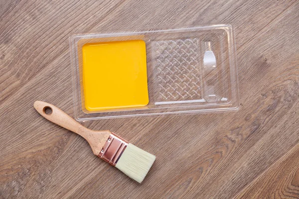 Closeup cuvette pintor com tinta amarela no chão marrom de madeira , — Fotografia de Stock