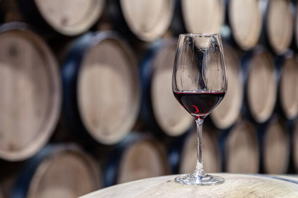 Closeup glass with red wine on background wooden wine oak barrel