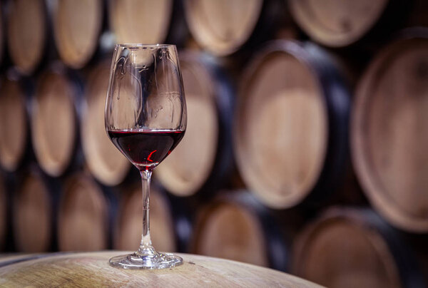 Closeup glass with red wine on background wooden wine oak barrel