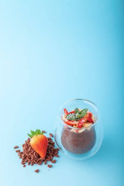 Çikolatalı Chia pudingi mavi arka planda çilekle süslenmiş.