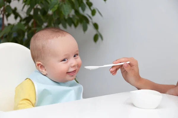 Primera alimentación del bebé, comer yogur, boca sucia, sostiene la cuchara —  Fotos de Stock