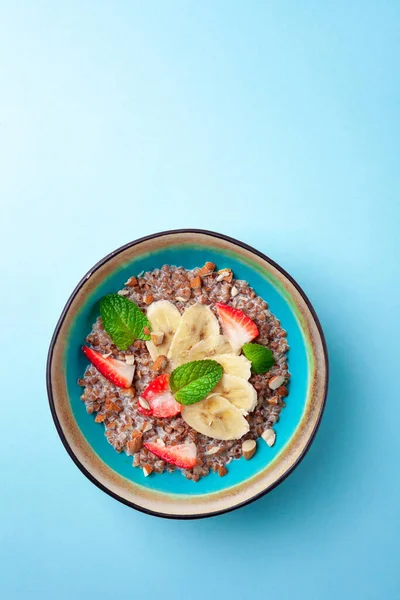 Bowl of milk buckwheat porridge with banana, nuts, strawberries, mint