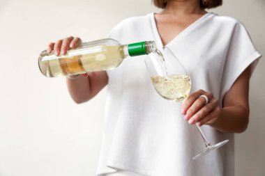 Kadın elleri şişeden cama beyaz şarap döker.