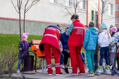 Rusya Kemerovo 2019-05-21 Ambulans Ekibi kırmızı üniformalı bir çocuğun apartmanın yanındaki bankta oturmasına yardım ediyor.