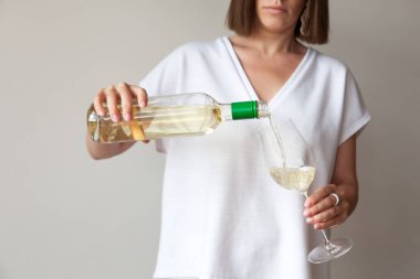 Kadın elleri şişeden cama beyaz şarap döker.