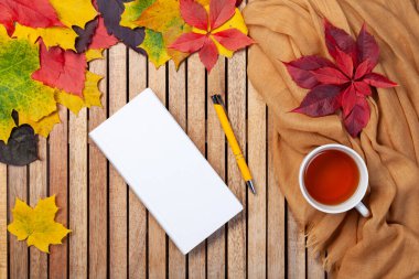 Sonbahar yaprakları, beyaz defter, masada çay fincanı, tekstil peçete, ahşap zemin