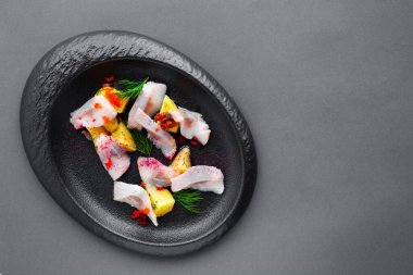 Soğuk meze tuzlu ringa balığı ve siyah tabakta haşlanmış patates.