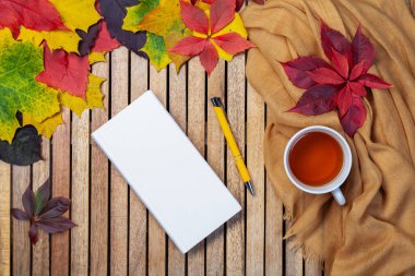 Sonbahar yaprakları, beyaz defter, masada çay fincanı, tekstil peçete, ahşap zemin