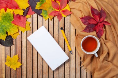 Sonbahar yaprakları, beyaz defter, masada çay fincanı, tekstil peçete, ahşap zemin