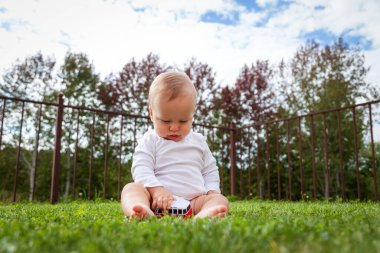 Komik sarışın bebek çimenlerde oturuyor ve oyuncaklarla oynuyor.