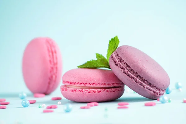 Pink and purple macaroons with mint leaves on blue background.