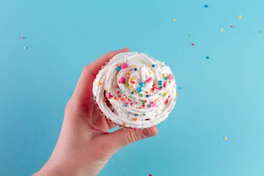 Muffin krema ve parlak toz ile parlak bir arka plan üzerinde tutan el 