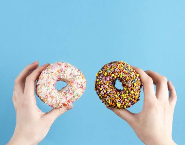 Mavi bir arka plan üzerinde elinde iki renkli donut